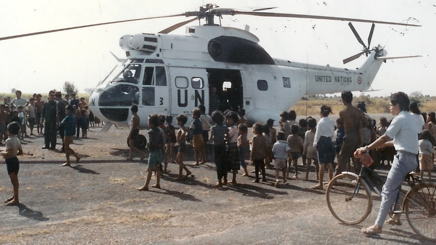 A big white United Nations helicopter resting on the ground, surrounded by Cambodian children.