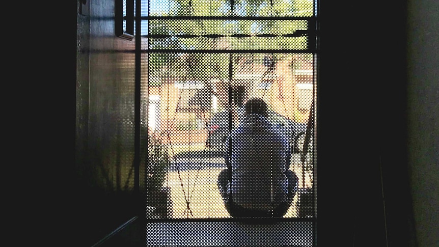 Photo through the front door looking out of John sitting on his front step with back to camera