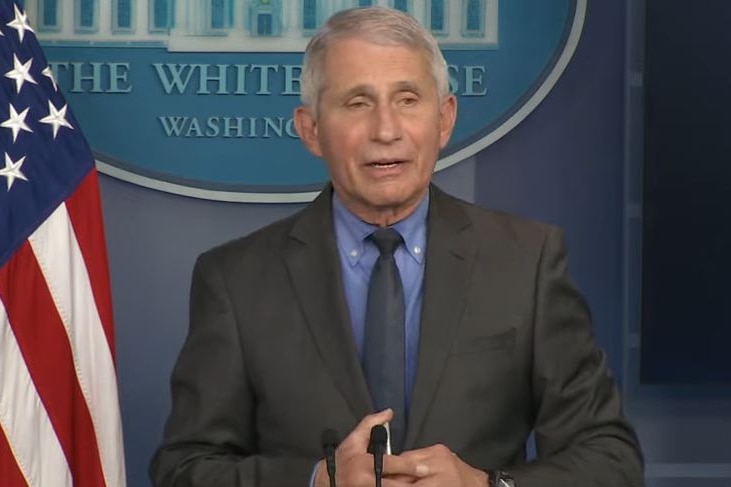 A man in a suit with a White House insignia and the American flag behind him.