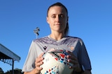 A woman faces the camera while holding a soccer ball.