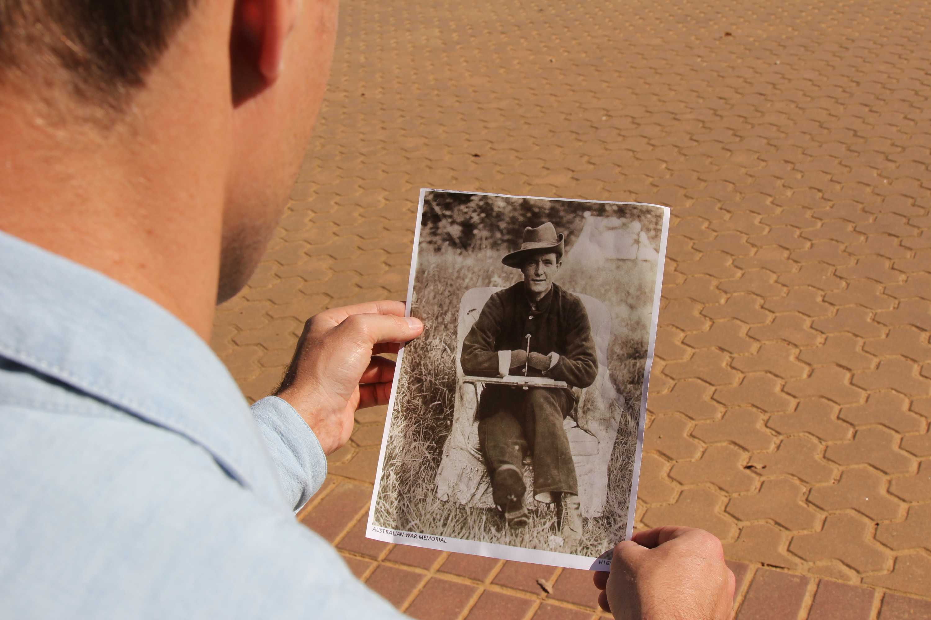 A man holds a photo of an unknown World War I soldier, who is missing his hands, from the Australian War Memorial collection.