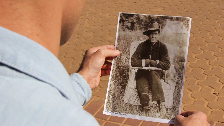 A man holds a photo of an unknown World War I soldier, who is missing his hands, from the Australian War Memorial collection.