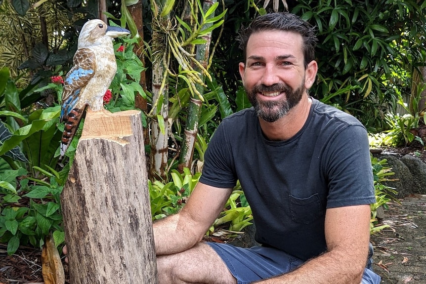 Man squatting beside log which has a kookaburra carved out of the top of the log