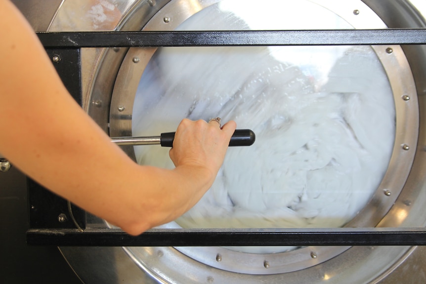 A  close-up of a front-loading washing machine, with an arm closing the door and towels visible inside