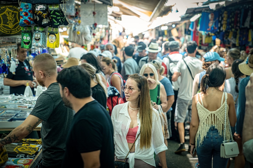 A young woman in a white shirt and pink crop top walks through a packed outdoor marketplace 