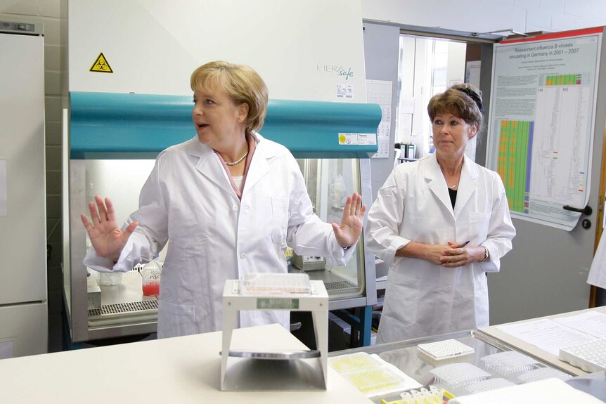 Angela Merkel in a lab coat surrounded by scientists