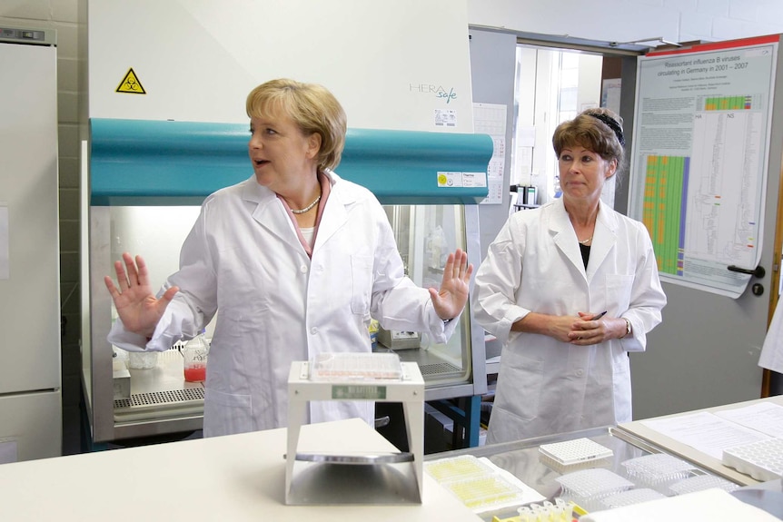 Angela Merkel in a lab coat surrounded by scientists