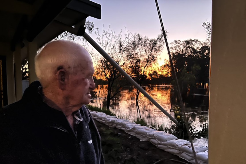 Old man looks at river flooding behind sandbag levee at sunset. NSW Flood 2022