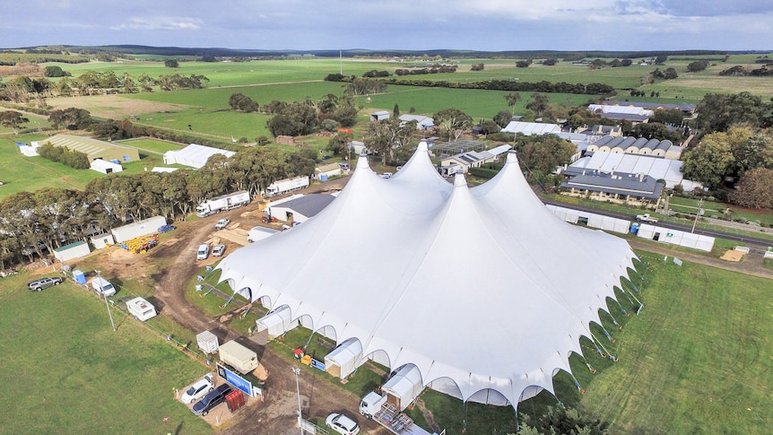 A giant big top tent sits in a paddock surrounded by portable offices, trucks and cars.