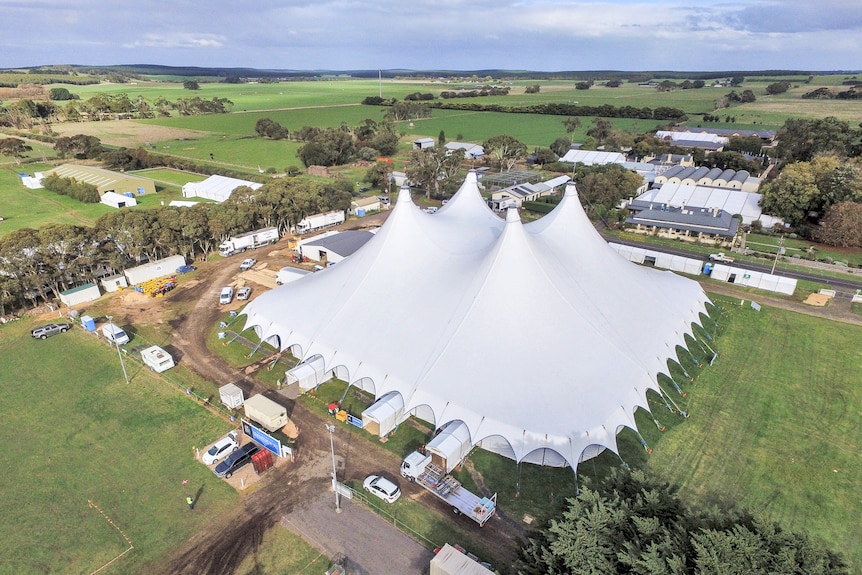 A giant big top tent sits in a paddock surrounded by portable offices, trucks and cars.