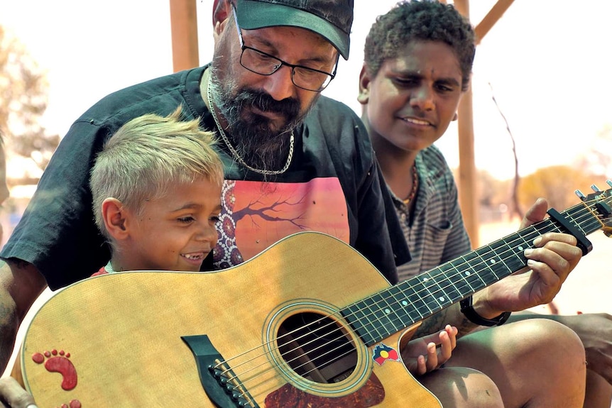 Young engagement officer Robert Binsiar shows a young boy from Yulga Jinna how to play the guitar.