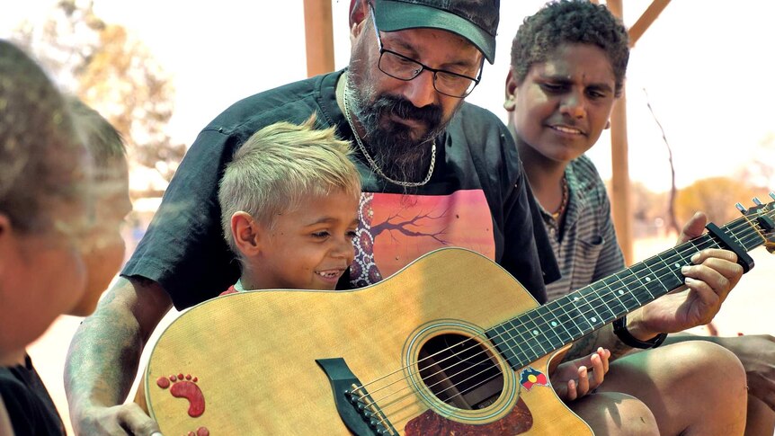 Young engagement officer Robert Binsiar shows a young boy from Yulga Jinna how to play the guitar.