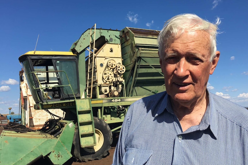 A man with white hair standing in front of a harvester.