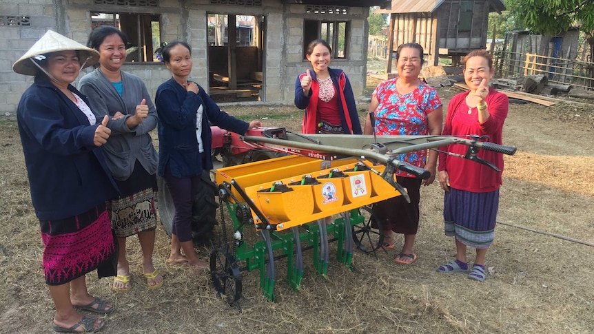 Female farmers stand with a new rice seeder.