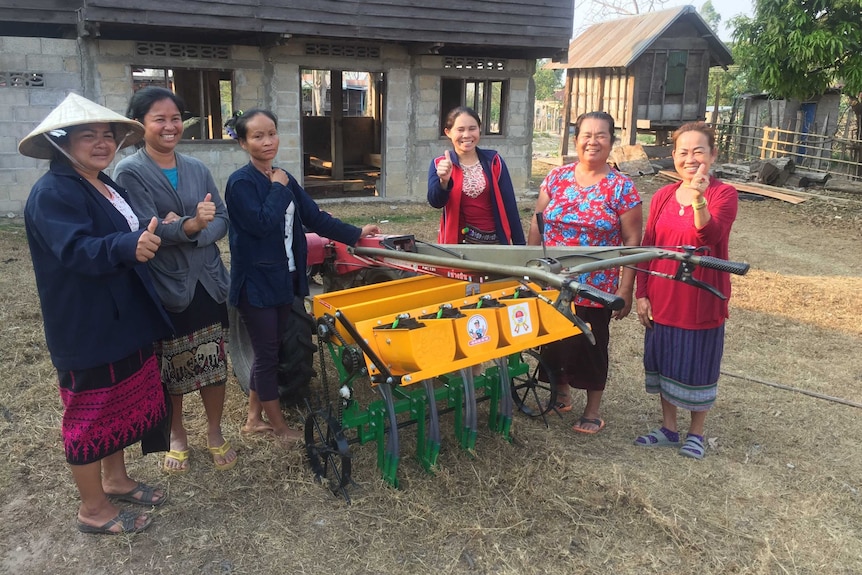 Female farmers stand with a new rice seeder.