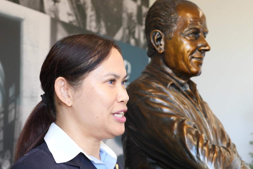 Woman on left head and shoulders close up, side angle, with bronze statue man's bust in background