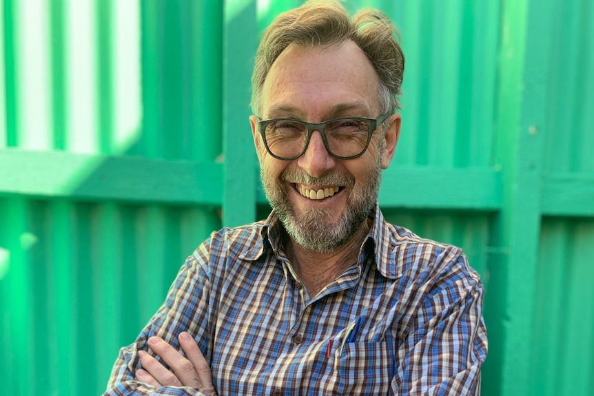 A man in a checked shirt and glasses laughs.