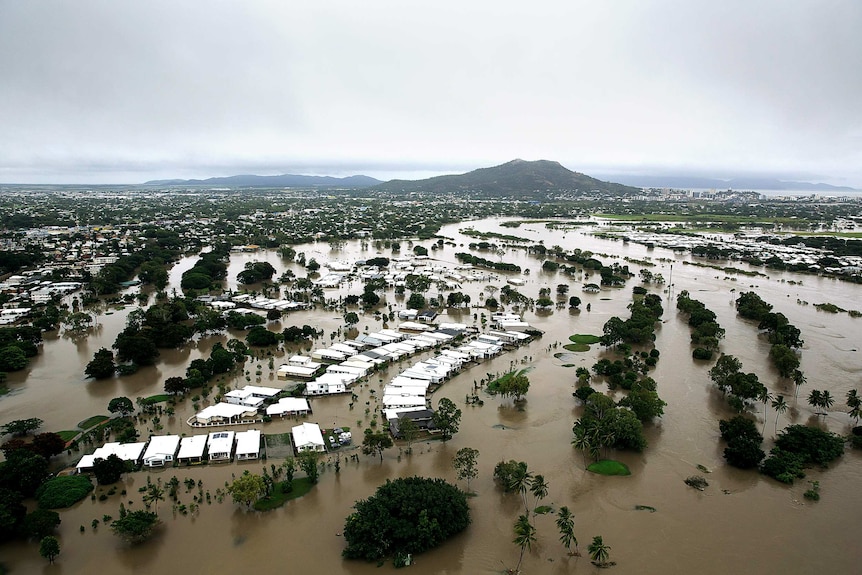 An aerial view of homes surrounded by brown water under overcast skies.