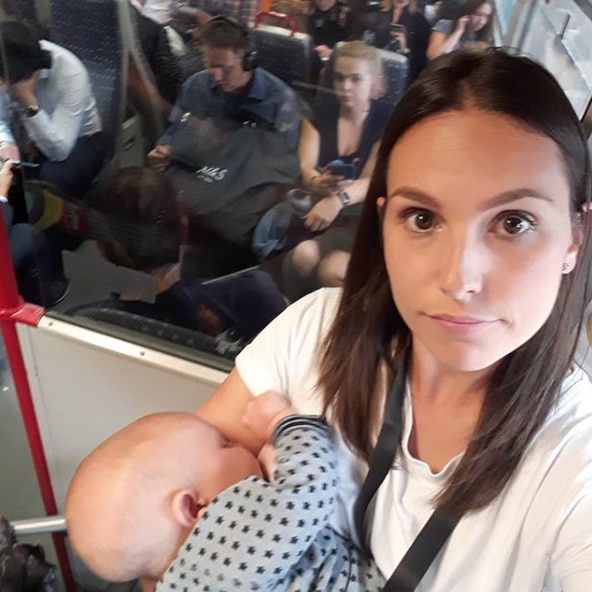 A mother looks at the camera angry while she stands and breastfeeds her baby on a busy train.