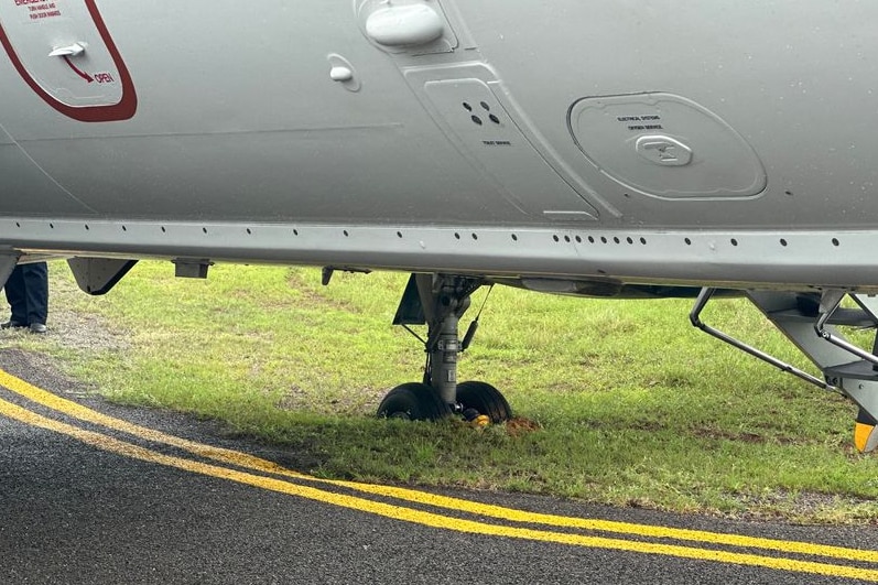 The wheel of a plane noticeably stuck in grass slightly of the tarmac of a runway
