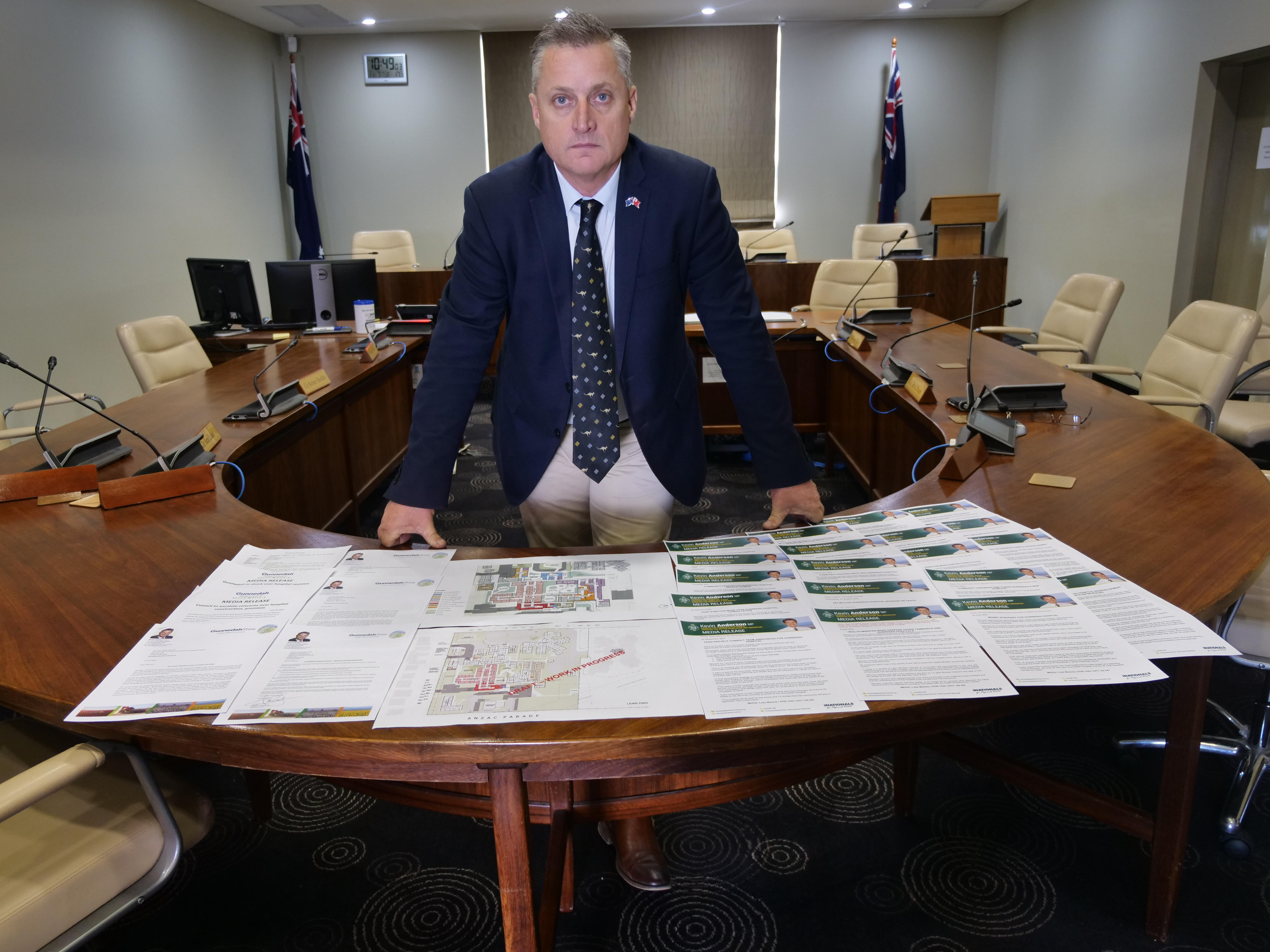 A man leans over building drawings with a stern expression on his face