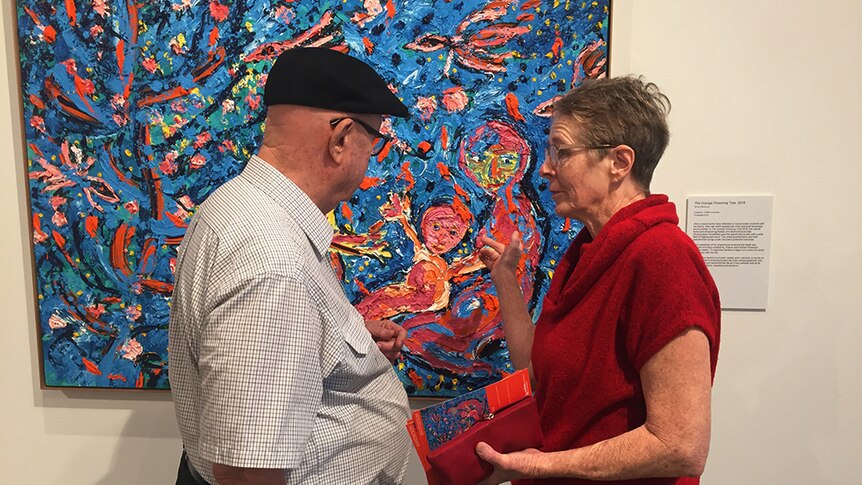 William Robinson and Davida Allen standing in front of a vibrant blue, pink and orange oil painting.