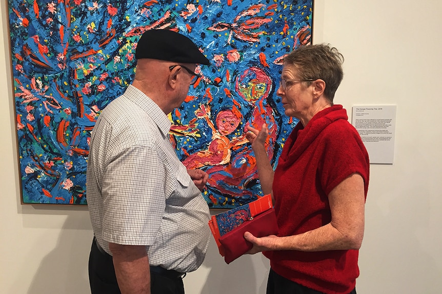 William Robinson and Davida Allen standing in front of a vibrant blue, pink and orange oil painting.