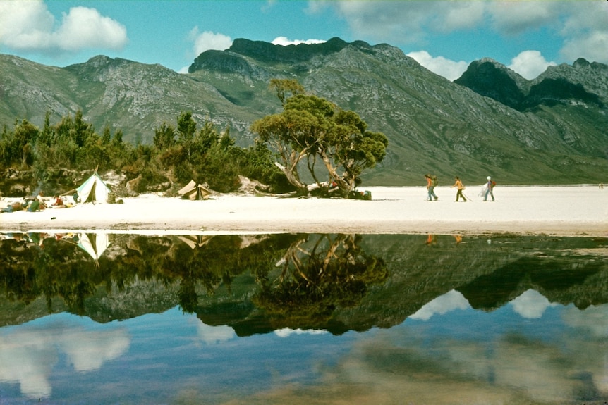 People camping on the edge of a lake, with mountains in the background.