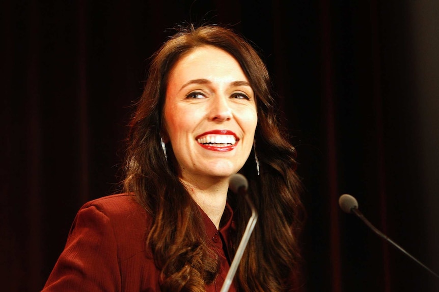 New Zealand's Labour Party leader Jacinda Ardern smiles under bright lights at a podium