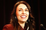 New Zealand's Labour Party leader Jacinda Ardern smiles under bright lights at a podium