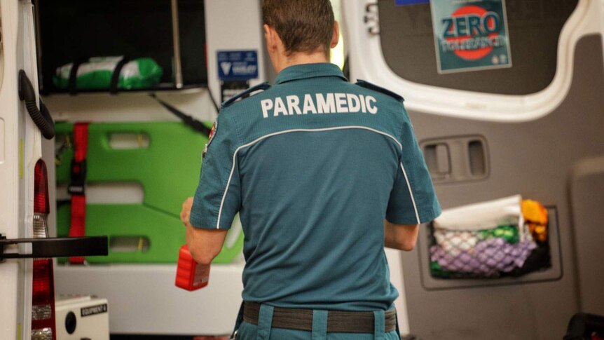 A Queensland paramedic stands at the back of an ambulance.