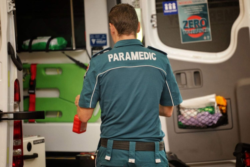 A Queensland paramedic stands at the back of an ambulance.