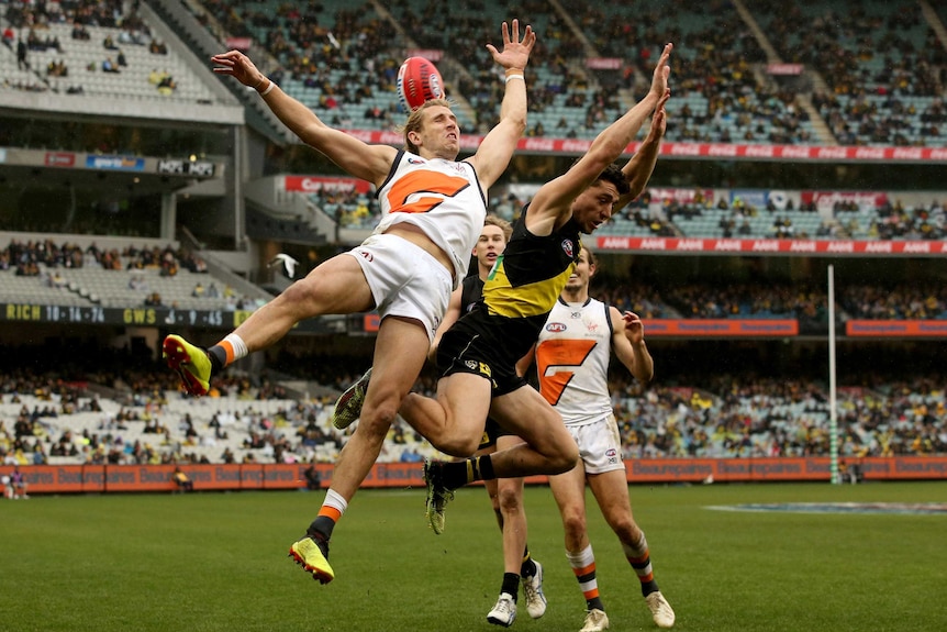 Two players collide, with the arms and legs going everywhere, as the ball goes over the top of them.