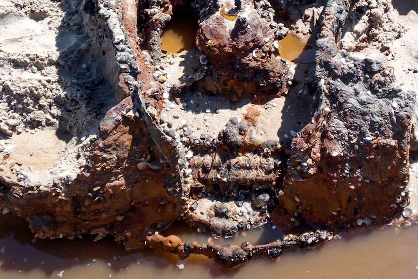 The front part of a rusty vintage car buried in the sand.
