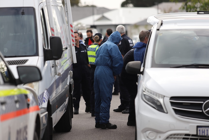 A forensics officer puts a suit between two vans as other police stand around.