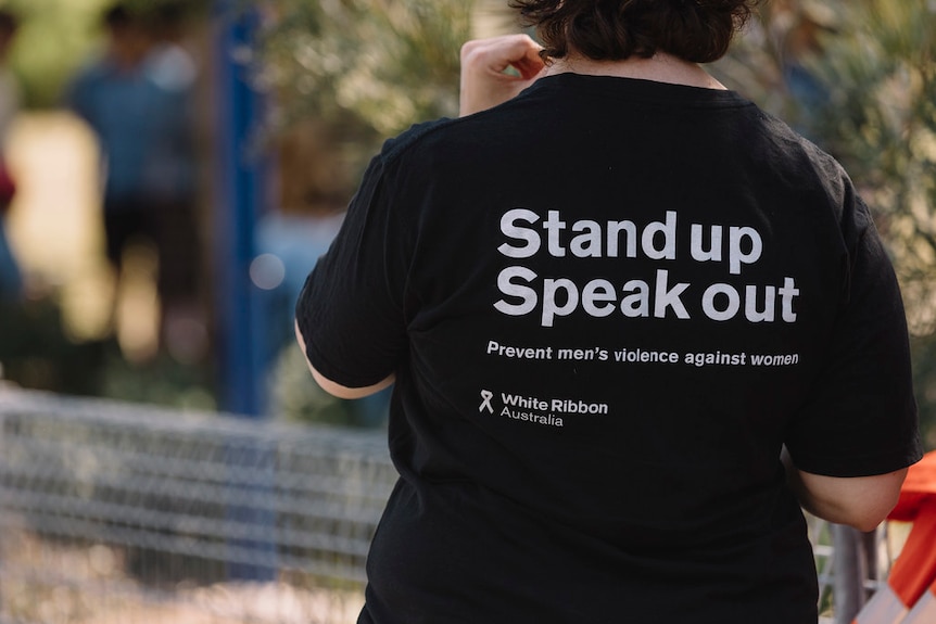 The back of a woman who is wearing a black t-shirt with white writing on it for White Ribbon Day