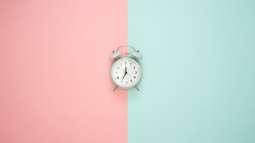 A small, wind-up clock sitting on a pink and green background.