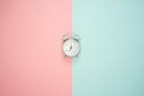 A small, wind-up clock sitting on a pink and green background.