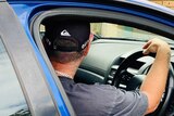 A man in a black cap sits in the driver's seat of a blue car