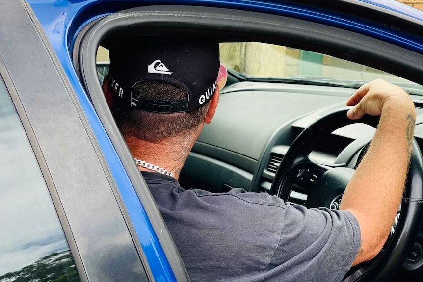 A man in a black cap sits in the driver's seat of a blue car