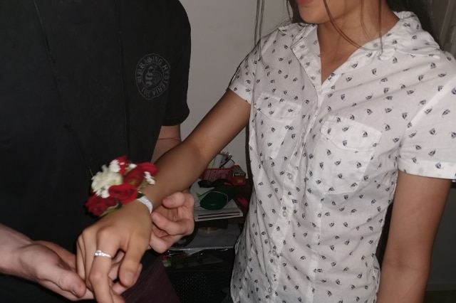 A man holds a woman's hand which has a corsage wrapped around it with red and white flowers on it.