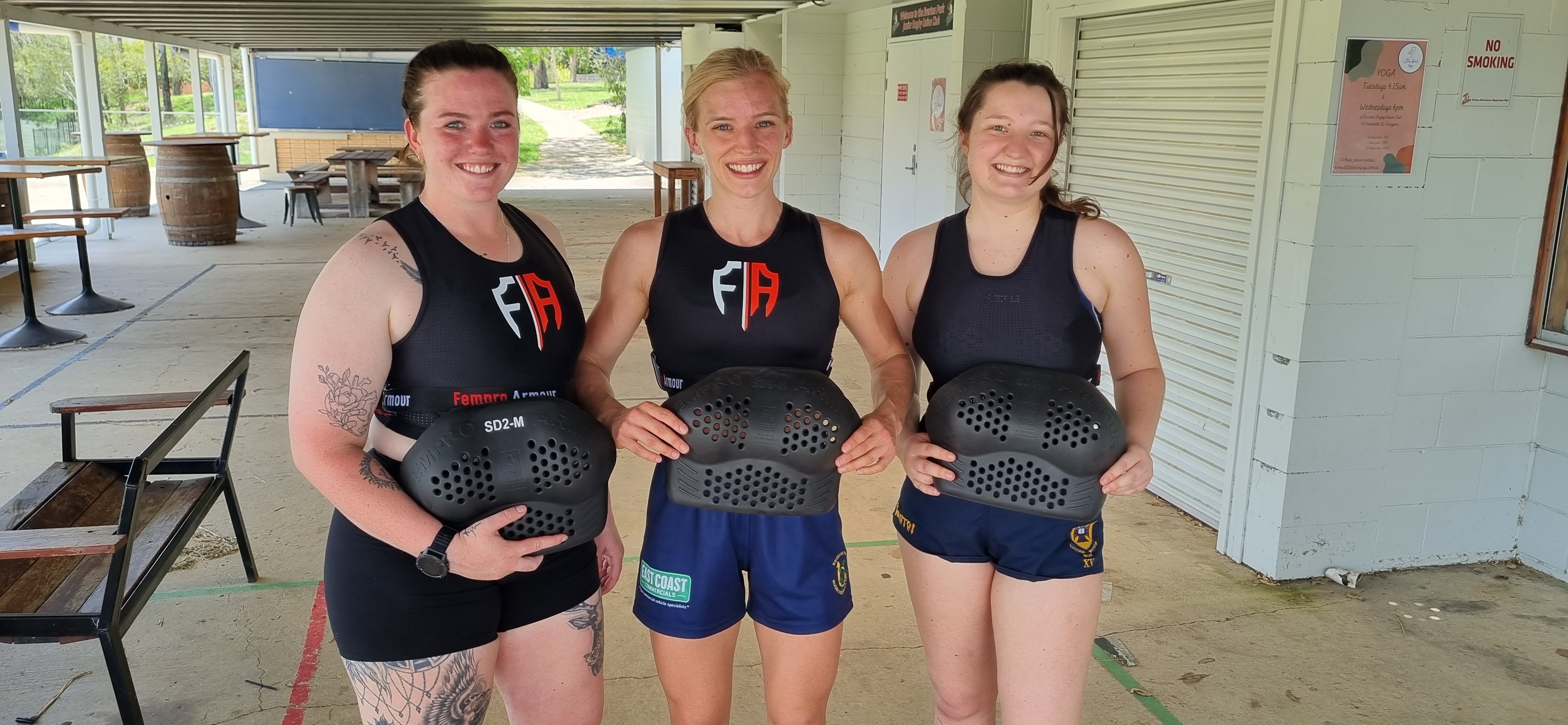 Three women hold up the sporting armour