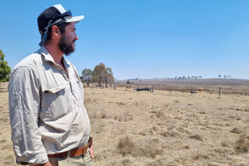 A man stands in a paddock, looking out across the landscape.