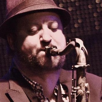 Aaron Searle in a fedora playing a tenor saxophone