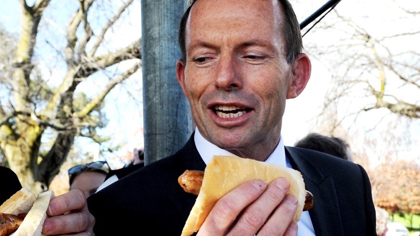 Tony Abbott with a sausage on bread at a community barbeque