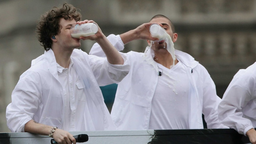 Two men dressed in white messily drinking milk.