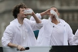Two men dressed in white messily drinking milk.