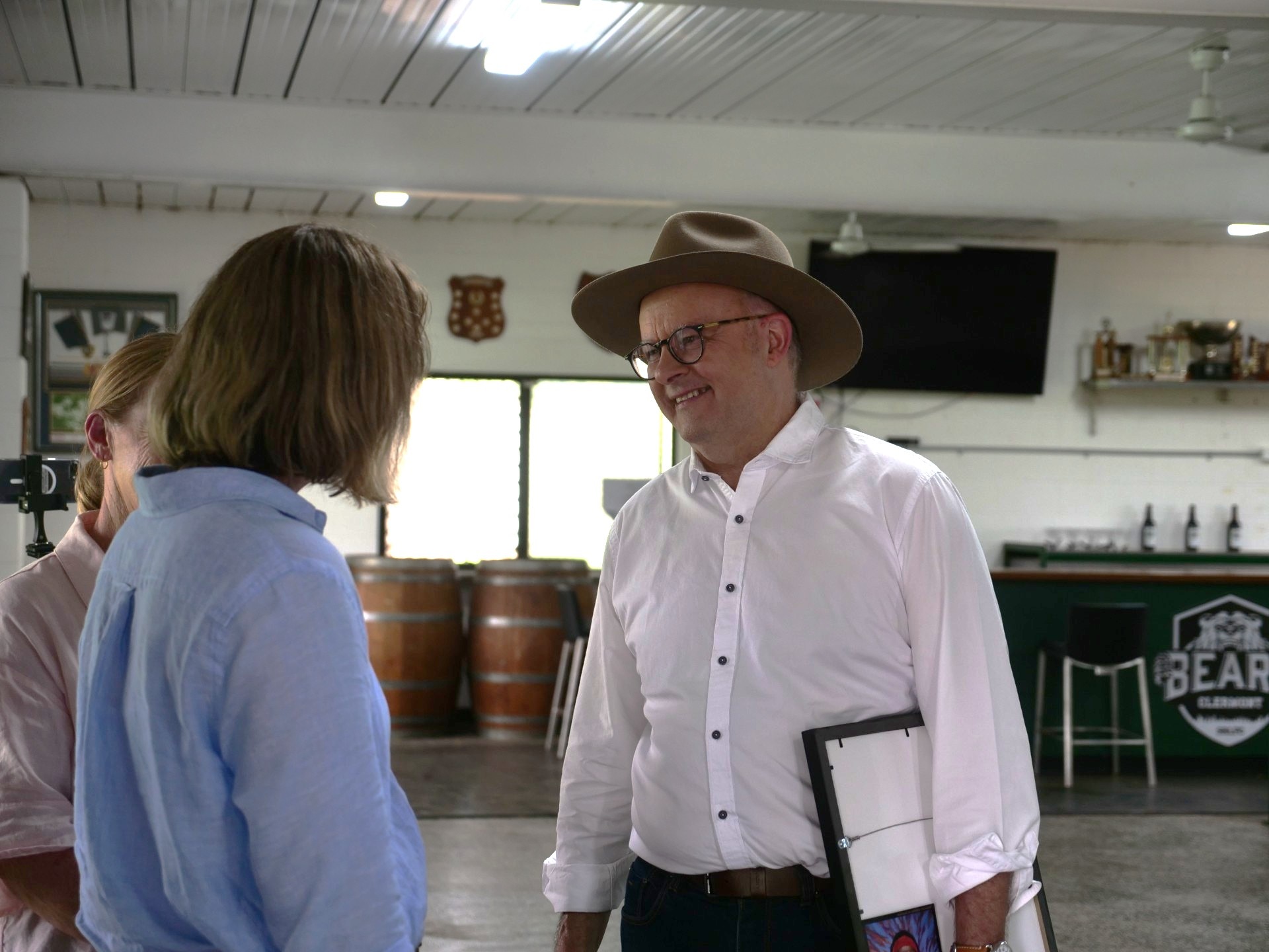 Anthony Albanese usa chapéu e conversa com uma mulher vestida de azul em um corredor.