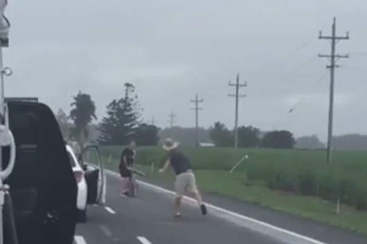 Two men play cricket on one lane of road with cars backed up on the other.