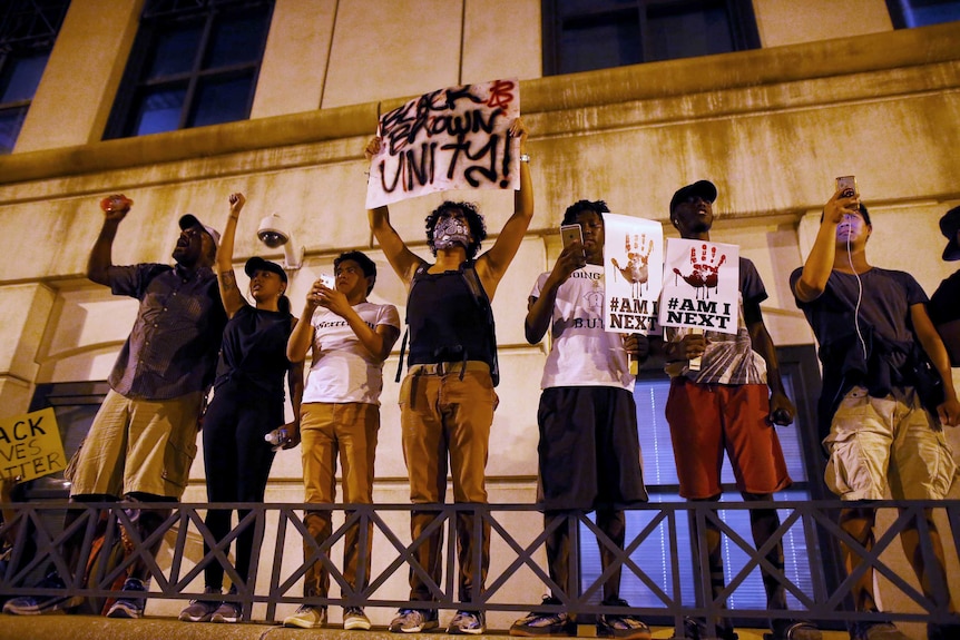 Protesters stand outside building holding protest signs
